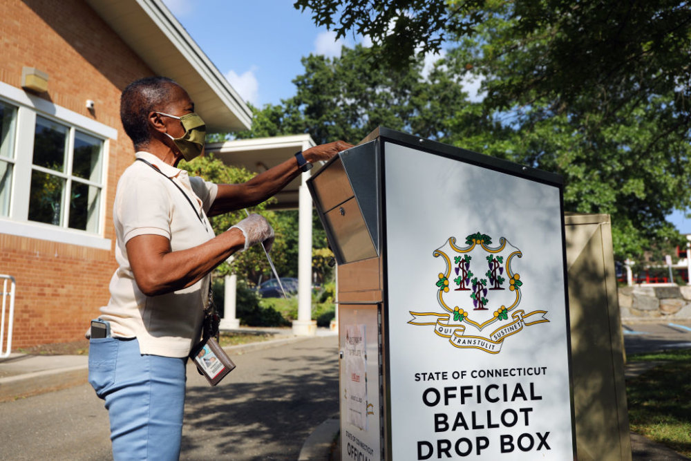 STAMFORD, CONNECTICUT - AUGUST 11: A woman drops her Connecticut 2020 presidential primary ballot at a secure ballot drop box at a Stamford library on August 11, 2020 in Stamford, Connecticut. Due to the ongoing COVID-19 pandemic, Connecticut Governor Ned Lamont signed an executive order allowing all registered voters to vote absentee in the August 11, 2020 primary. Connecticut has also experienced fallout from the recent tropical storm, which knocked out power to half of the state at its peak. President Trump has been critical of the absentee ballot process saying it contributes to voter fraud.  (Photo by Spencer Platt/Getty Images)