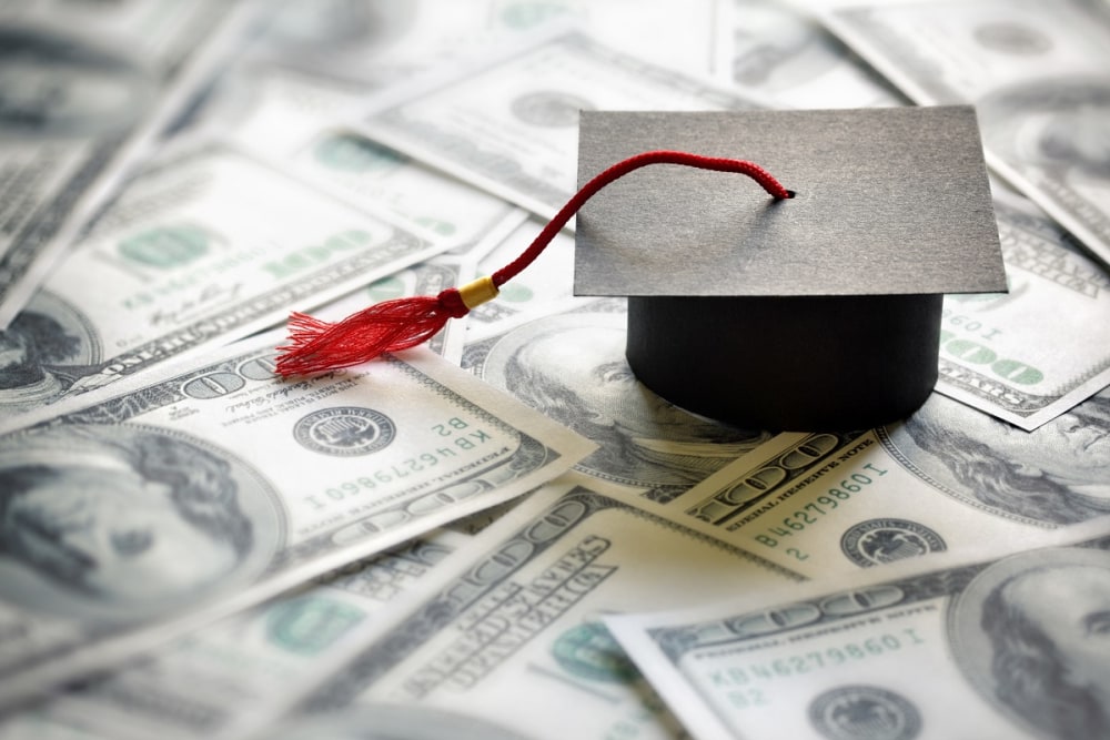 Graduation cap on table of $100 bills