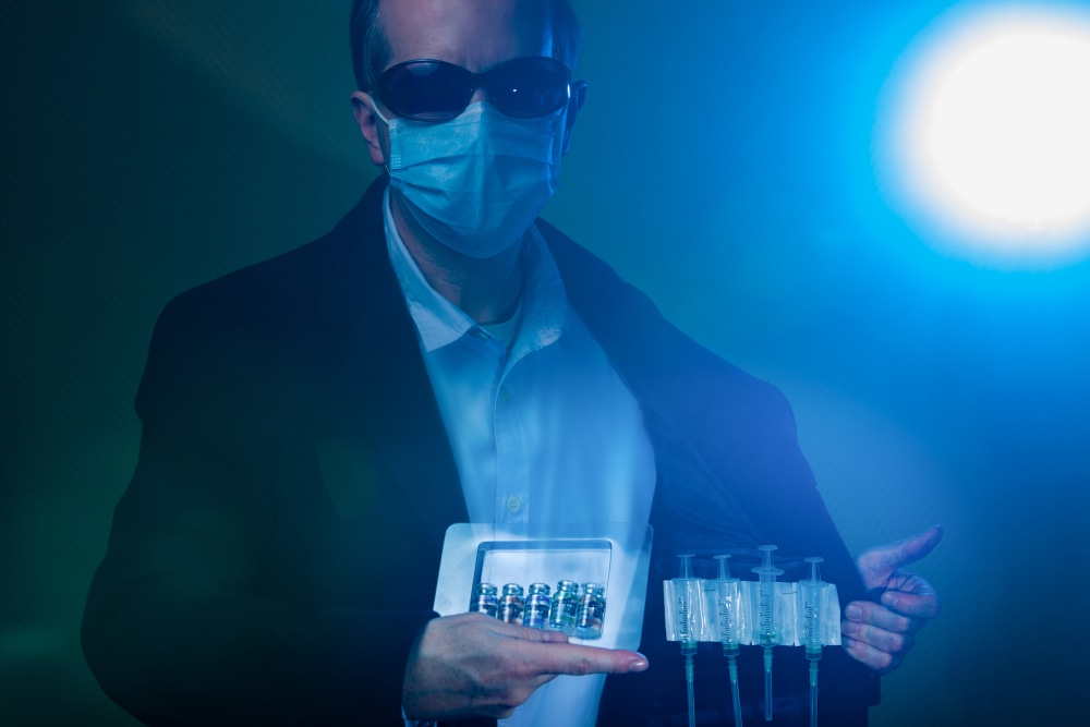Suspicious man in suit, wearing a surgical protective face mask and sunglasses. Deals in fake illegal COVID-19 (SARS-CoV-2) Coronavirus vaccine vials and injection syringes. Opens jacket and shows hidden syringes and a box of vaccine bottles.Note: QR code on bottles was generated by me and contains generic text: "SARS-CoV-2 Vaccine"