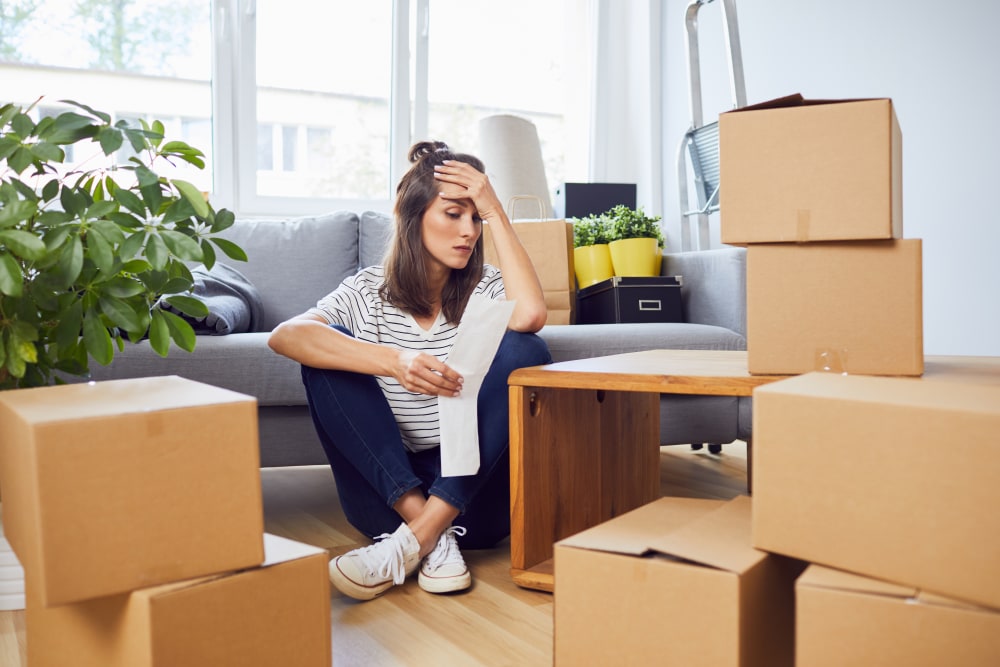 Worried young woman looking at bill sitting on floor in new apartment after moving in