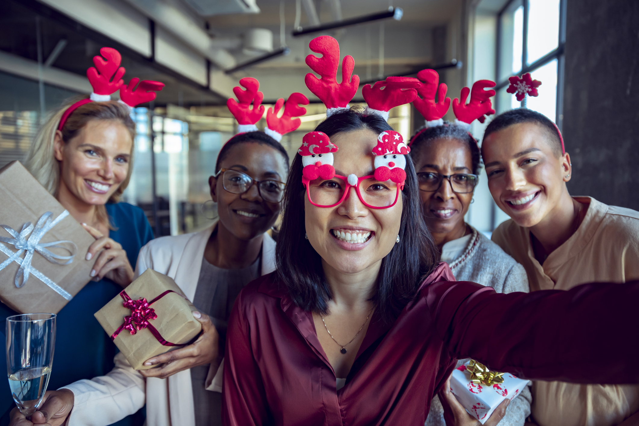 Coworkers wearing festive antlers pose for a selfie at a work holiday party