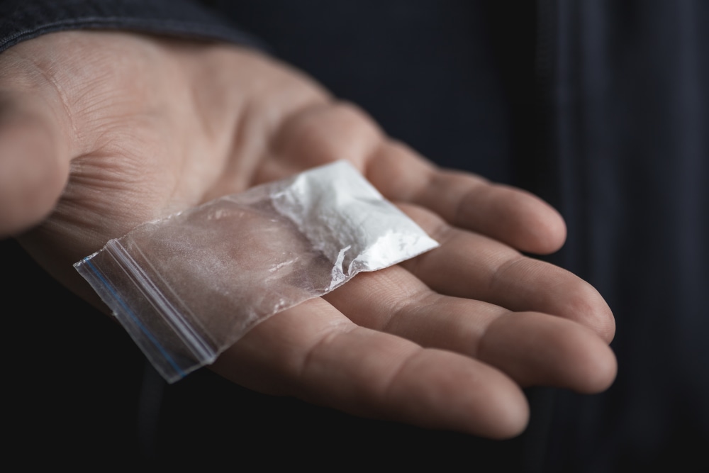 Hand holding on palm plastic packet with cocaine powder or other drugs